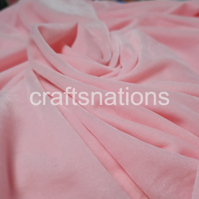 May include: A close-up of a soft, pink velvet fabric. The fabric is draped and folded, showing its texture and drape.