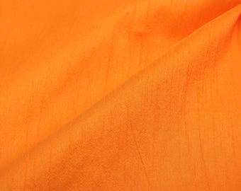 May include: A close-up of a bright orange fabric with a smooth, slightly textured surface. The fabric is folded in half, creating a diagonal line across the image.