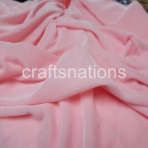 May include: A close-up of a soft, pink fabric with a subtle sheen. The fabric is draped and folded, showcasing its texture and drape.