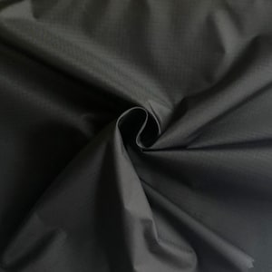 Peut inclure: Tissu noir avec une surface lisse et légèrement texturée. Le tissu est plié et drapé, montrant sa texture douce et fluide.