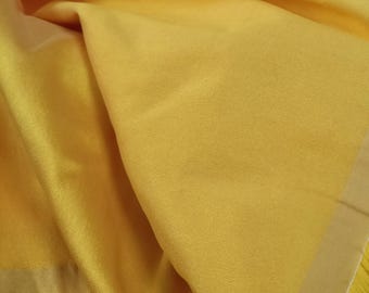 May include: A close-up of a yellow fabric with a smooth, silky texture. The fabric is folded and has a slight sheen.