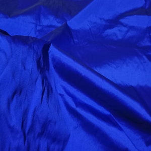 Può includere: Un primo piano di un tessuto blu liscio con una texture morbida e setosa. Il tessuto è piegato e drappeggiato, creando una sensazione di movimento e fluidità.
