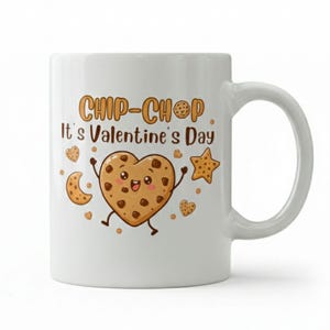 May include: White ceramic mug with a Valentine's Day design. The mug displays a cartoon heart-shaped cookie character with arms and legs, alongside other cookie shapes. Text on the mug reads "CHIP-CHOP It's Valentine's Day."