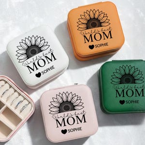 May include: A collection of personalized jewelry boxes in various colors: white, orange, pink, and green. Each box features a sunflower design and the text "World's best MOM" with a name and a heart symbol. One box is open, revealing jewelry.