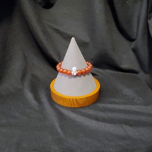 May include: A red carnelian beaded bracelet with a silver charm on a wooden display stand.