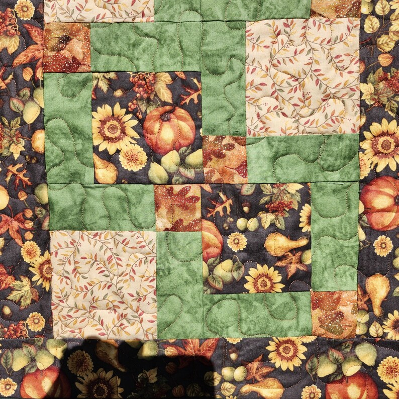Puede incluir: Un edred&oacute;n de retazos con un tema de cosecha de oto&ntilde;o. El edred&oacute;n muestra cuadrados de tela con girasoles, calabazas y hojas de oto&ntilde;o en tonos naranja, amarillo, verde y marr&oacute;n. El edred&oacute;n est&aacute; acolchado con una puntada ondulada.