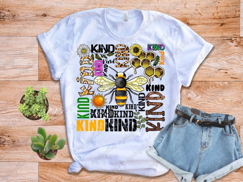 May include: White t-shirt with a bee and honeycomb design. The shirt has the word "Kind" repeated multiple times in different colors and fonts.