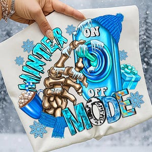 May include: White t-shirt with a winter theme design. The design includes the words "WINTER MODE" in blue, a skeleton hand, a blue switch with "ON" and "OFF", a blue hat, snowflakes, a mug of hot chocolate, and a blue scarf.