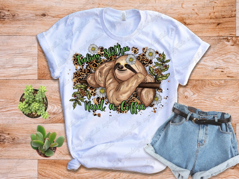 Puede incluir: Camiseta blanca con un gr&aacute;fico de un perezoso colgado de una rama con estampado de leopardo y flores. El texto "Feeling Slothful Need a Coffee" est&aacute; impreso en la camiseta.