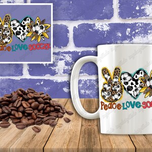 May include: White ceramic mug with a colorful design featuring a peace sign, heart, and sunflower, all with soccer ball patterns. The text "Peace Love Soccer" is printed on the mug.