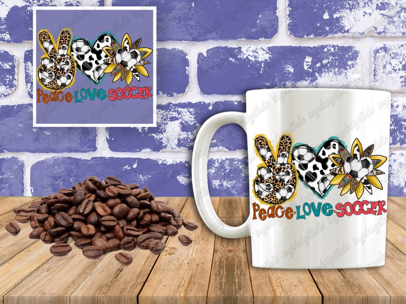 May include: White ceramic mug with a colorful design featuring a peace sign, heart, and sunflower, all with soccer ball patterns. The text "Peace Love Soccer" is printed on the mug.