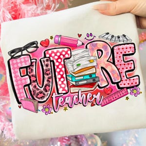 May include: Cream-colored sweatshirt with the words "FUTURE TEACHER" in a colorful design. The design includes glasses, a pencil, books, hearts, a ruler, and flowers. The letters have various patterns.