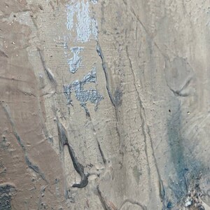 May include: Abstract painting with a textured, layered surface. The painting features shades of gray, brown, and blue, with a silver metallic accent.