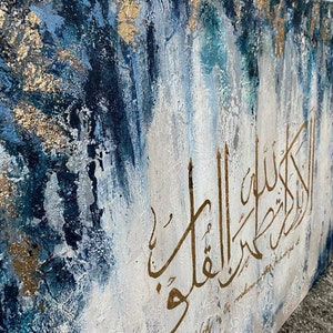 May include: Abstract painting with a blue, white, and gold color scheme. The painting features Arabic calligraphy in gold paint with the text "Verily in the remembrance of Allah"
