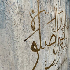 May include: A white canvas with a textured surface features gold calligraphy in Arabic script. The text reads "Love & help those around you".