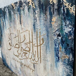 May include: Abstract painting with blue, white, and gold paint. The painting features Arabic calligraphy in gold paint. The text reads "And help those who are patiently praying."