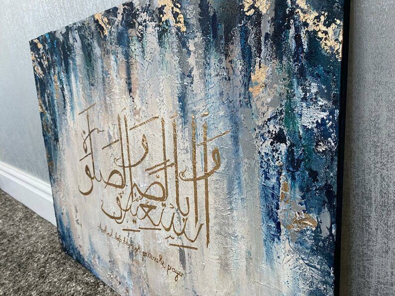 May include: Abstract painting with blue, white, and gold paint. The painting features Arabic calligraphy in gold paint. The text reads "And help those who are patiently praying."