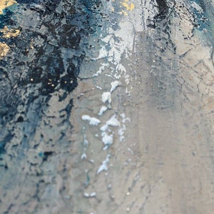 May include: Abstract painting with a textured surface. The painting features shades of blue, gray, and gold. The paint is applied in a thick, layered style, creating a sense of depth and movement.