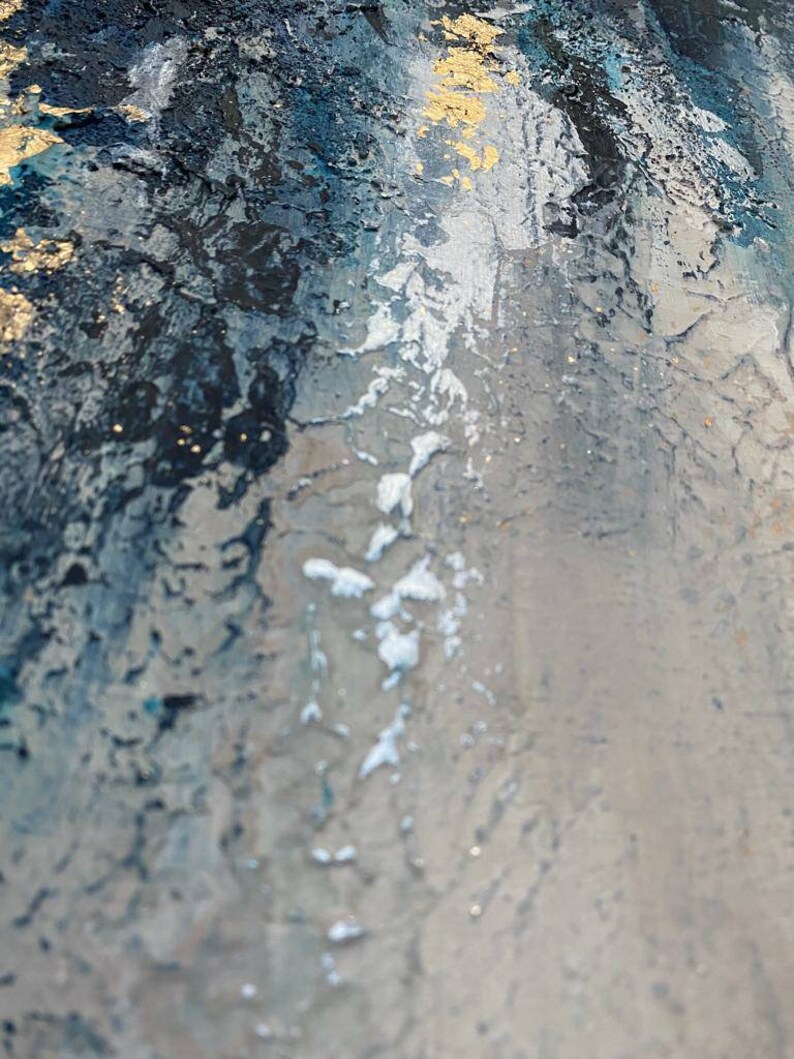 May include: Abstract painting with a textured surface. The painting features shades of blue, gray, and gold. The paint is applied in a thick, layered style, creating a sense of depth and movement.