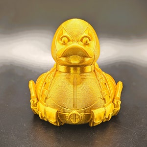 以下が含まれることがあります： デッドプールデザインの金色のゴム製アヒル。アヒルは、黒い目の赤いマスクと、デッドプールのロゴが付いた黒いベルトをしています。