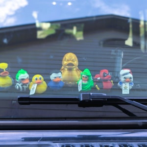 以下が含まれることがあります： 金色のアヒル、緑色のアヒル、赤色のアヒル、青色のアヒル、黄色のアヒル、白いアヒルのゴム製のおもちゃのセットが、車のフロントガラスに飾られています。