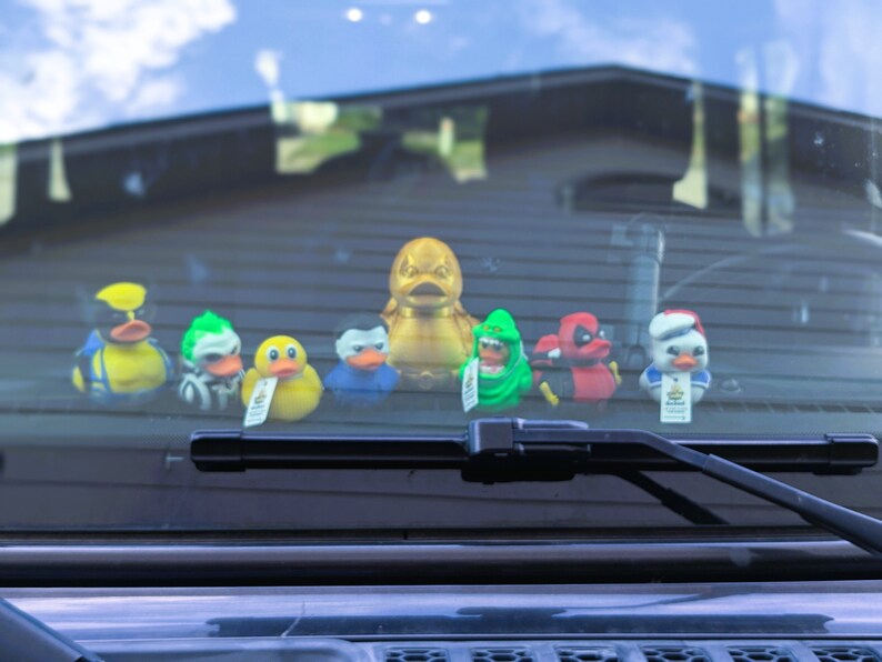 以下が含まれることがあります： 金色のアヒル、緑色のアヒル、赤色のアヒル、青色のアヒル、黄色のアヒル、白いアヒルのゴム製のおもちゃのセットが、車のフロントガラスに飾られています。
