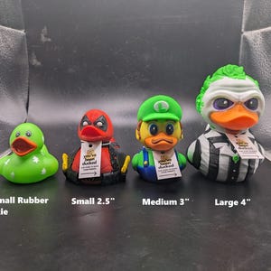 以下が含まれることがあります： 異なるサイズとデザインのゴム製アヒル4匹。最も小さいアヒルは白の星がついた緑色、次は赤と黒のデッドプールデザイン、次は緑と黄色のマリオデザイン、そして最も大きいのは緑と白のビートルジュースデザイン。各アヒルには「You've been ducked」と書かれたタグが付いています。