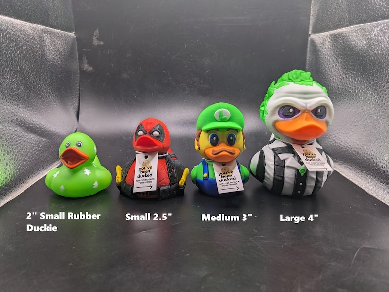 以下が含まれることがあります： 異なるサイズとデザインのゴム製アヒル4匹。最も小さいアヒルは白の星がついた緑色、次は赤と黒のデッドプールデザイン、次は緑と黄色のマリオデザイン、そして最も大きいのは緑と白のビートルジュースデザイン。各アヒルには「You've been ducked」と書かれたタグが付いています。