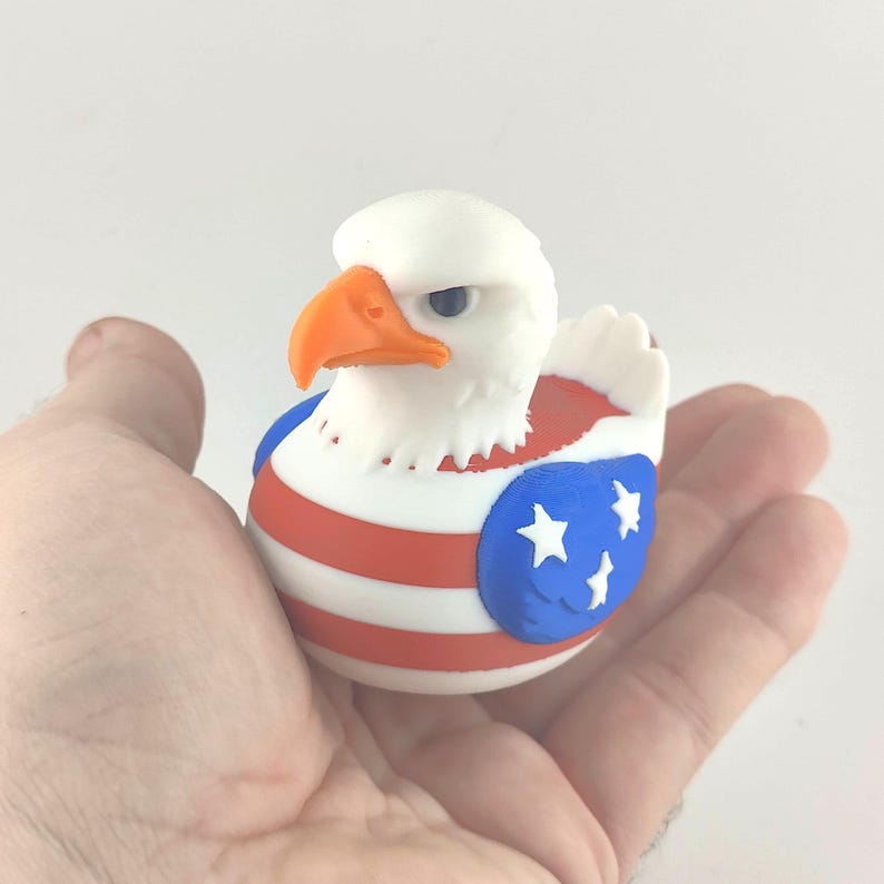 May include: A novelty rubber duck in the shape of a bald eagle, featuring a white head, orange beak, and a red, white, and blue design with stars. A quirky and patriotic item, perfect for collectors or as a gift.