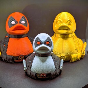 以下が含まれることがあります： 3つのゴム製のオモチャの鴨、それぞれ色が異なり、デザインも異なります。最初の鴨は赤と黒、2番目は白と黒、3番目は黄色と黒です。