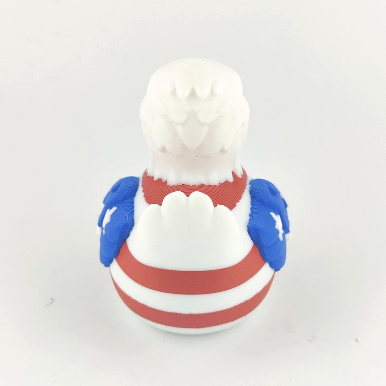 May include: A rubber duck decorated in the style of the American flag. It has a white head and chest, a red and white striped body, and blue wings with white stars. A novelty item.