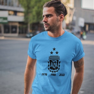 Pu&ograve; includere: Maglietta azzurra con un disegno nero raffigurante uno stemma con tre stelle, le lettere "AFA" e gli anni 1978, 1986 e 2022. La maglietta &egrave; a maniche corte e realizzata in materiale morbido.