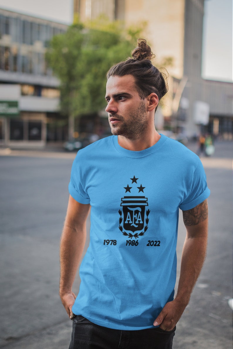 Pu&ograve; includere: Maglietta azzurra con un disegno nero raffigurante uno stemma con tre stelle, le lettere "AFA" e gli anni 1978, 1986 e 2022. La maglietta &egrave; a maniche corte e realizzata in materiale morbido.