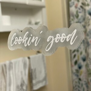 May include: A white sticker with the text "lookin' good" on a bathroom mirror.
