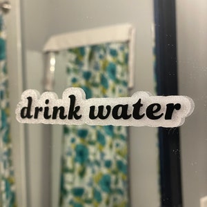 May include: A white bathroom mirror with a black framed border. A black vinyl sticker with the text "drink water" is on the mirror.