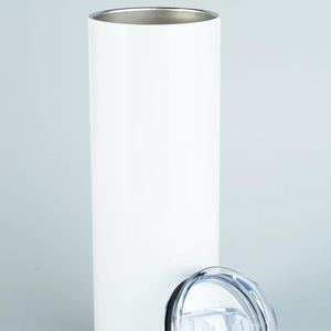 May include: A tall, cylindrical white tumbler with a smooth, matte finish and a metallic silver interior rim. The vessel is accompanied by a clear, circular plastic lid featuring a sliding closure mechanism and a black rubber gasket seal.