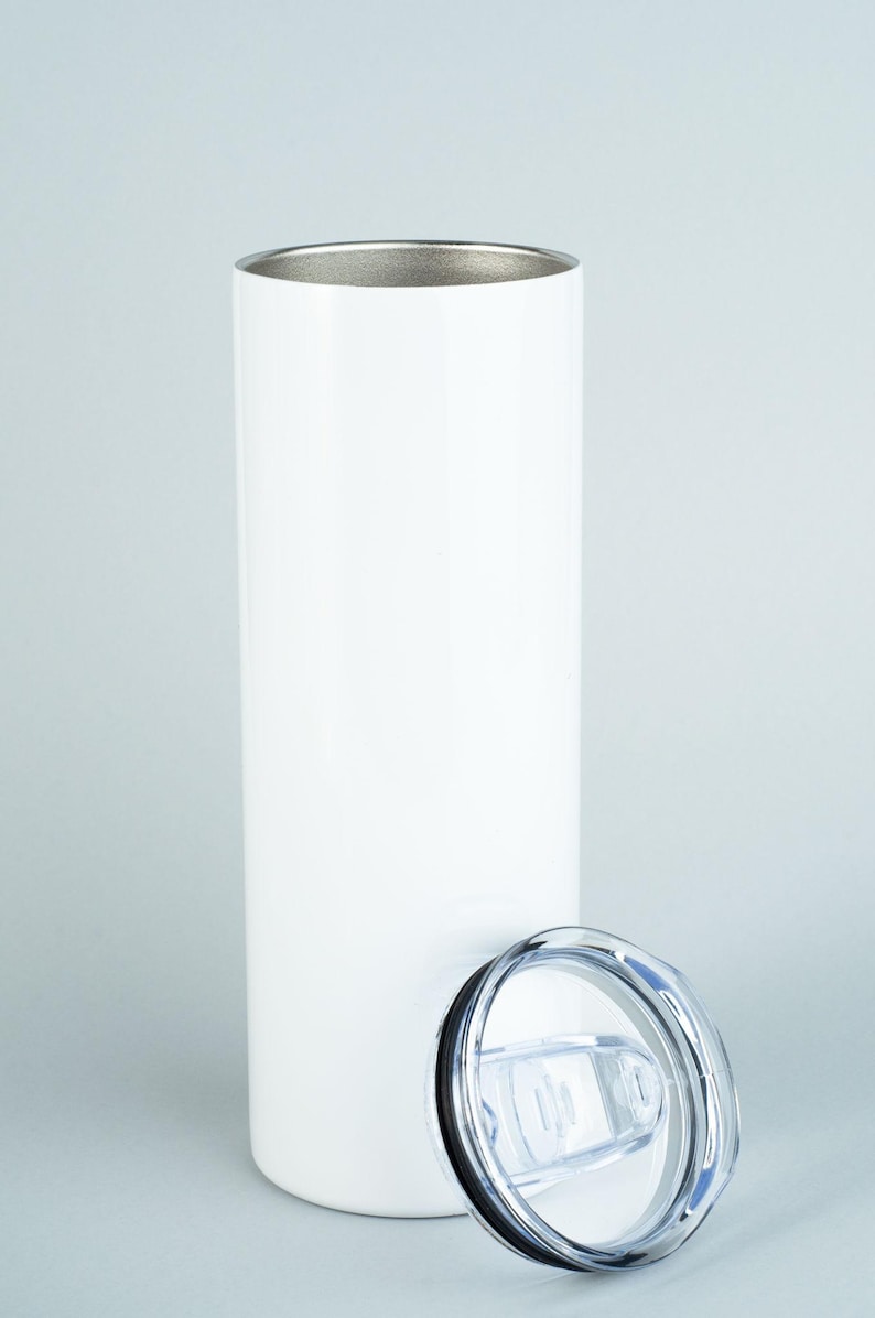 May include: A tall, cylindrical white tumbler with a smooth, matte finish and a metallic silver interior rim. The vessel is accompanied by a clear, circular plastic lid featuring a sliding closure mechanism and a black rubber gasket seal.