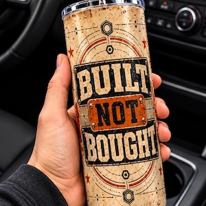 May include: A cylindrical stainless steel tumbler with a clear lid and a metal straw. The exterior features a distressed beige background with orange and black geometric accents, stars, and the bold text "BUILT NOT BOUGHT" in a block font.