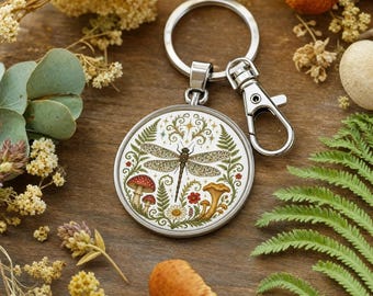 Portachiavi a forma di libellula, in acrilico, con elementi naturali come felci e funghi.