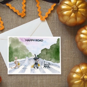 May include: A watercolor illustration of a Halloween-themed card with the text "HAPPY ROAD" and a depiction of a ghost, witch, and mummy crossing a street.