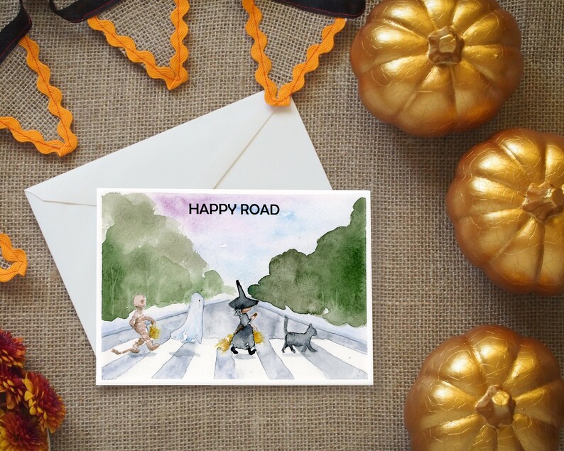 May include: A watercolor illustration of a Halloween-themed card with the text "HAPPY ROAD" and a depiction of a ghost, witch, and mummy crossing a street.