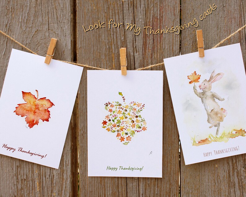 May include: Three Thanksgiving cards with watercolour illustrations. The first card features a single orange and red leaf. The second card features a cluster of leaves in the shape of a bell. The third card features a rabbit holding a leaf. All cards have the text "Happy Thanksgiving!"