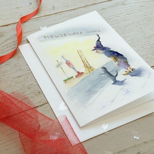 May include: A watercolor illustration of a witch wearing a purple hat and black dress, walking past a store with a sign that reads "Houseware Store".