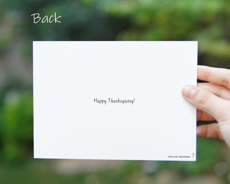 May include: A white card with the text "Happy Thanksgiving!" written in black ink. The card is blank on the front and has the name "SMADAR GROSSMAN" printed in the bottom right corner.