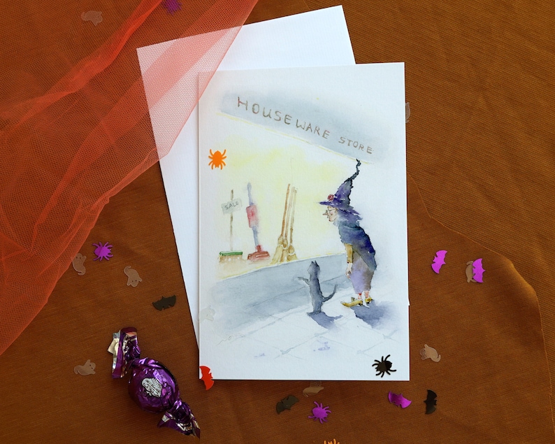 May include: A watercolor illustration of a witch with a black cat in front of a store called "Houseware Store". The witch is wearing a purple robe and a pointed hat. The cat is black and white.