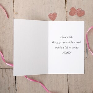 May include: A white card with a pink ribbon and pink glitter hearts. The card reads "Dear Kate, May you be a little scared and have lots of candy! XOXO"
