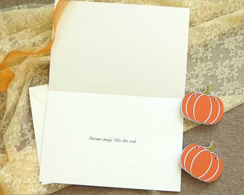 May include: A blank card with a white envelope and two orange pumpkin decorations. The card has the text "Autumn magic fills the soul" written on the inside.