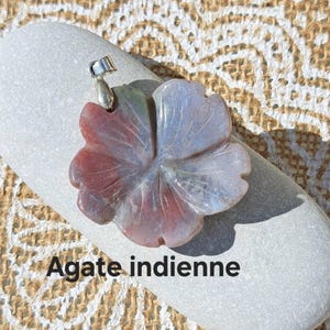 Op de afbeelding: Een bloemvormige hanger gesneden uit Indiase agaat, met tinten rood, grijs en wit. De hanger heeft een zilverkleurige balein om aan een ketting te bevestigen. De tekst "Agate indienne" is zichtbaar onderaan de afbeelding.