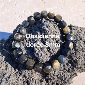 Puede incluir: Un brazalete de obsidiana dorada con cuentas de 8 mm. El brazalete se exhibe sobre una superficie oscura y texturizada. Las cuentas tienen un corte facetado, que refleja la luz y muestra las variaciones naturales de color.