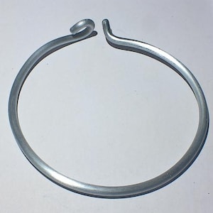 May include: A silver metal ring with a simple design. The ring is open and has a slight bend at the top.